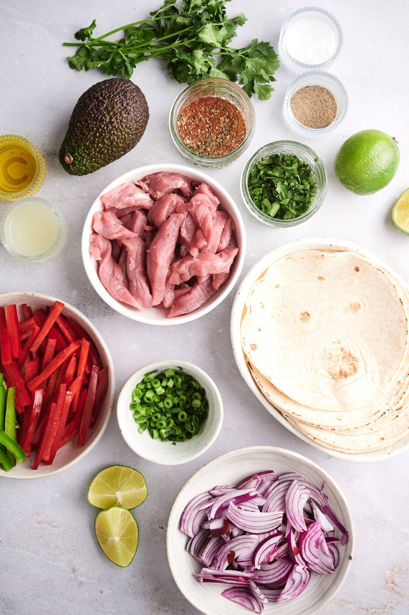 Ingredients for pork fajitas including pork tenderloin, bell peppers, red onions, fajita seasoning, limes, olive oil, and cilantro.