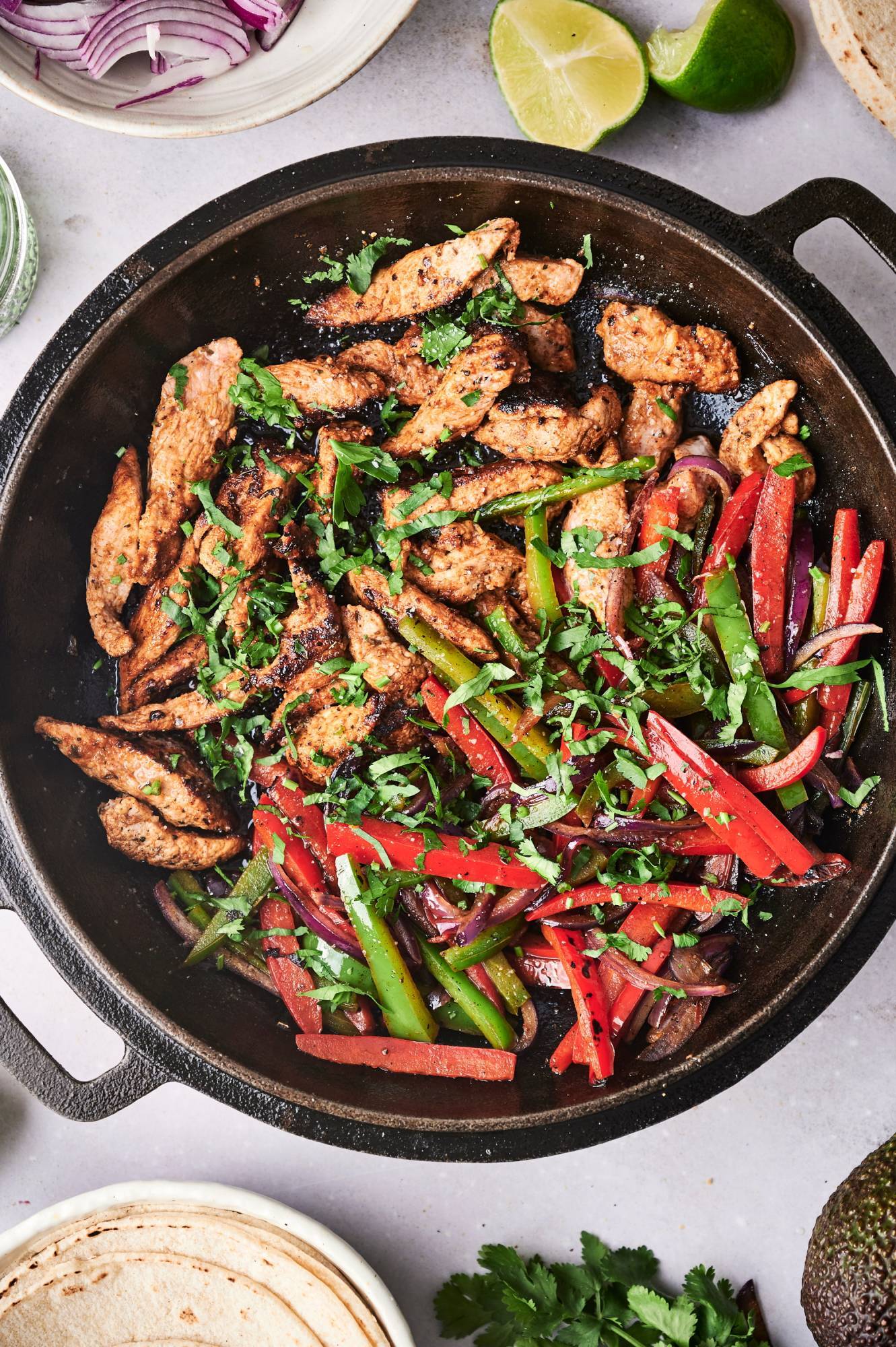 Pork tenderloin fajitas with seasoned pork, bell peppers, red onions, and cilantro in a cast iron skillet.