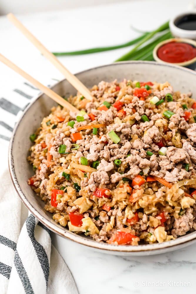 Cauliflower pork fried rice ground pork, vegetables, and chopsticks in a bowl with chop sticks.