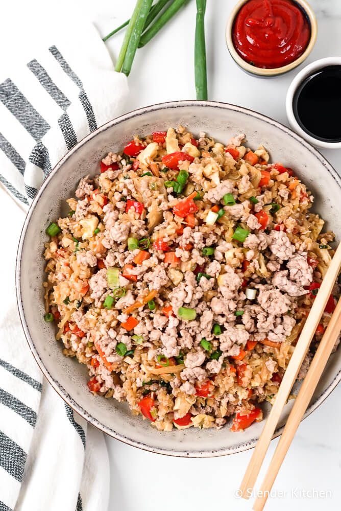 Cauliflower fried rice and ground pork, cabbage, carrots, and green onions in a bowl with soy sauce