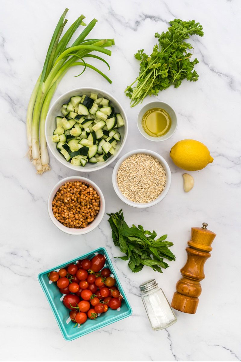 Ingredients for quinoa tabbouleh including parsley, quinoa, lentils, cucumbers, tomatoes, mint, and lemon.