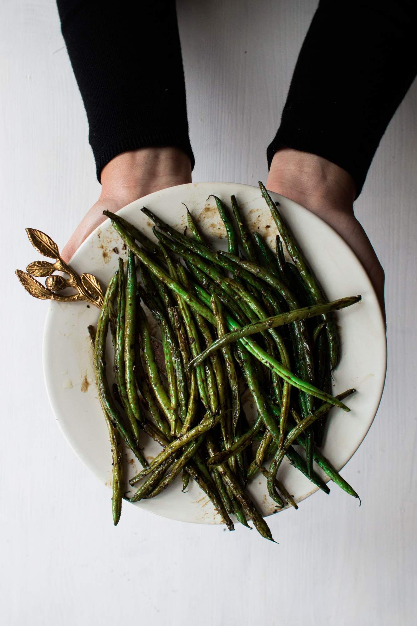 Roasted green beans on a plate with garlic and a gold leaf spoon.