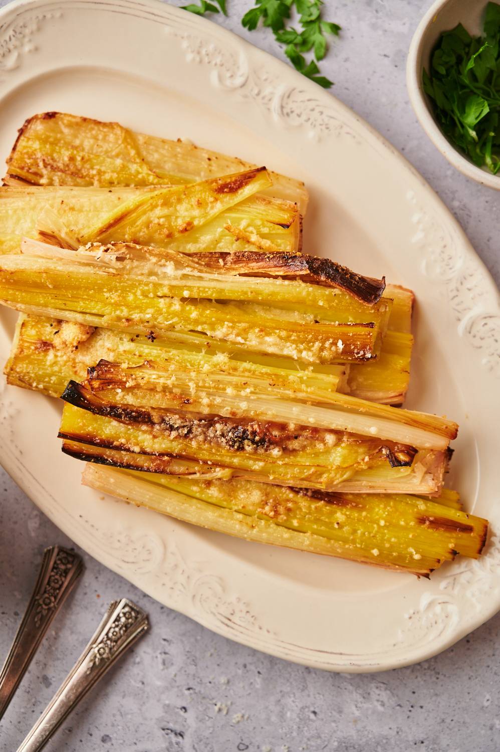 Plate with roasted leeks served with Parmesan cheese and fresh herbs.