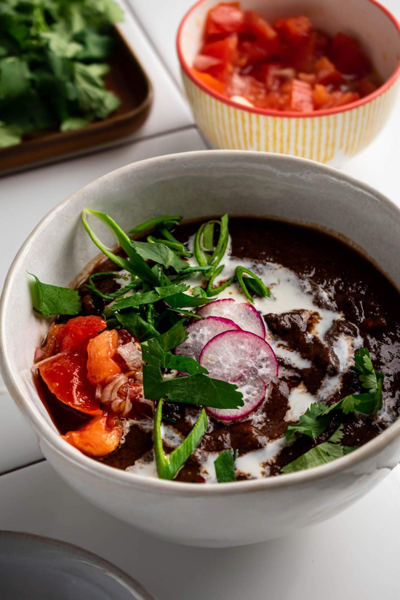 Black bean soup made in the crockpot served in a bowl with fresh cilantro, radishes, tomatoes, and sour cream.