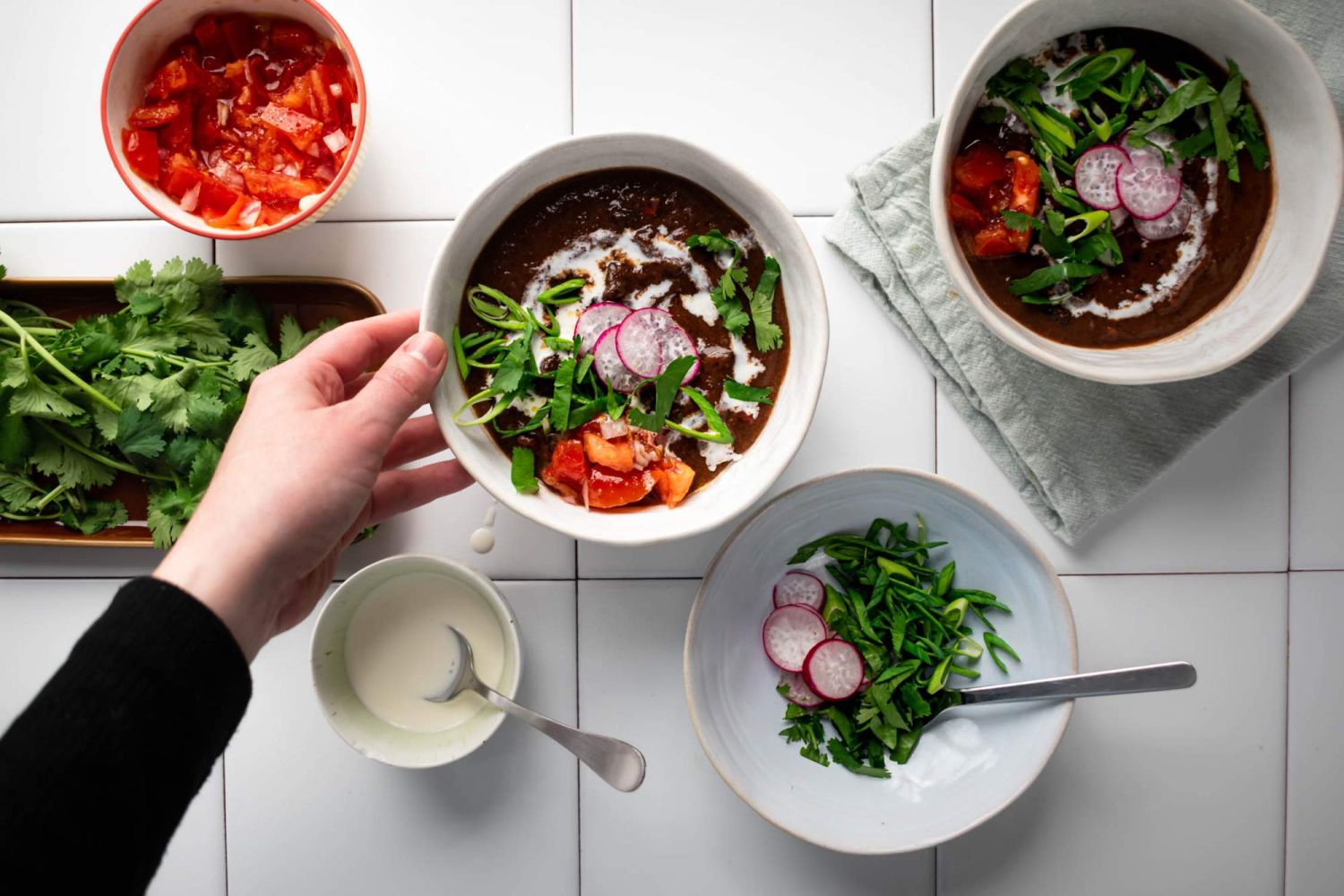 Crockpot black bean soup served in two bowls with tomatoes, cilantro, radishes, and sour cream on the side.