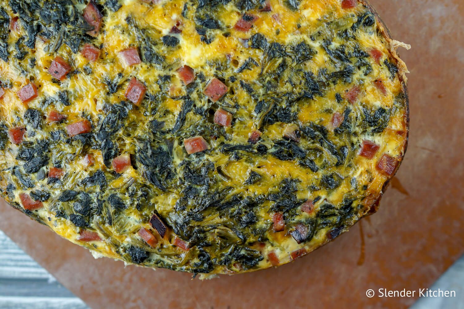 Slow Cooker egg breakfast casserole with spinach, ham, and cheese on a cutting board.