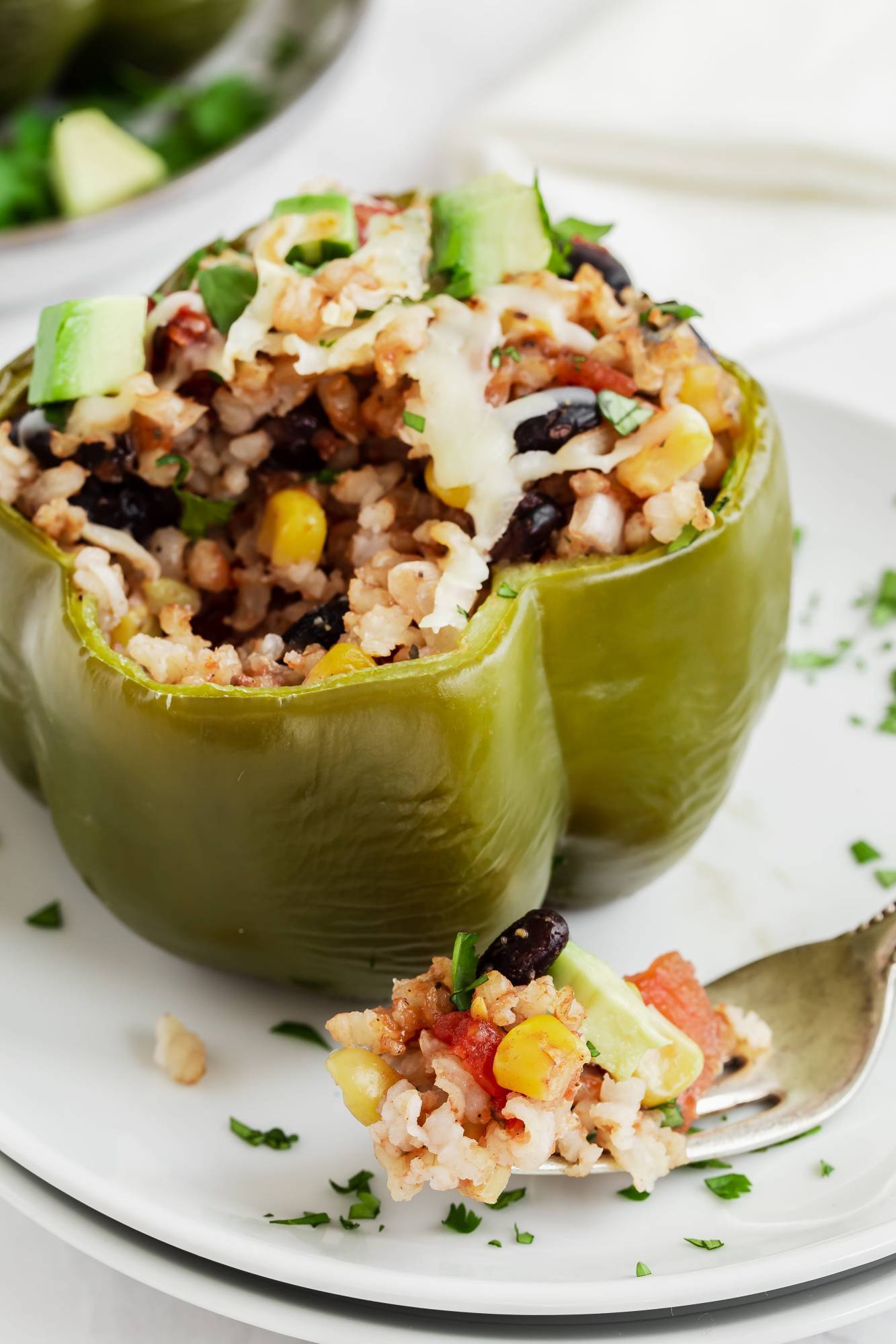 Stuffed green bell pepper with rice, corn, tomatoes, black beans, barbecue sauce, and avocado on a plate.