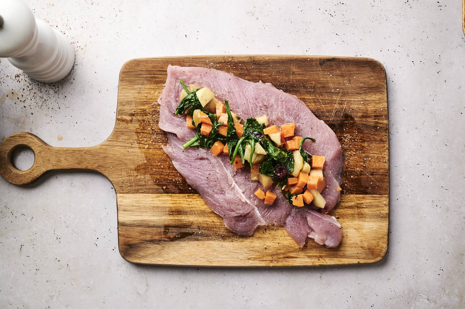 Butterflied turkey tenderloin stuffed with apples, sweet potatoes, spinach, and dried cranberries on a wooden cutting board.