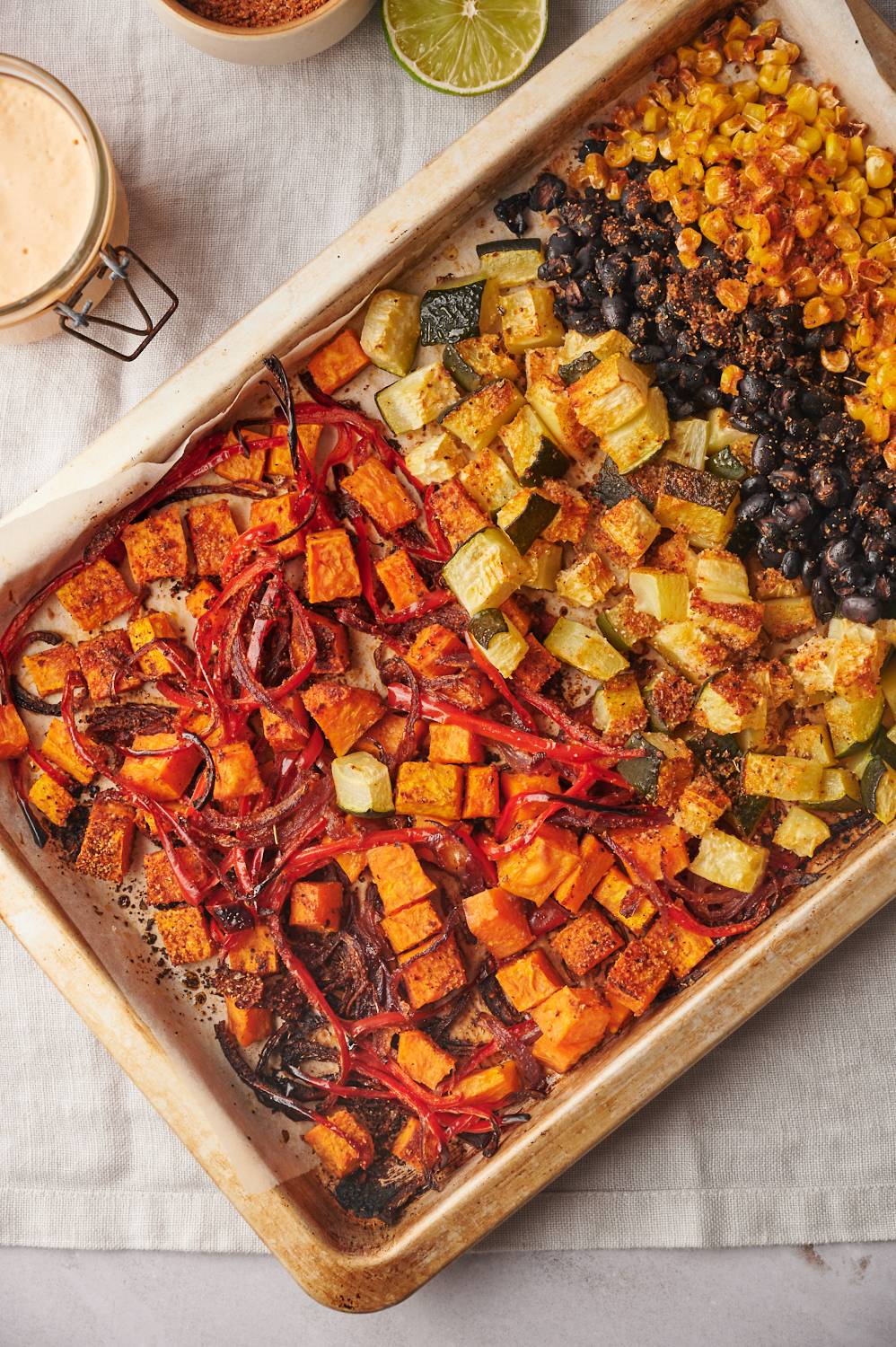 Roasted sweet potatoes, zucchini, black beans, corn, onions, and bell peppers on a sheet pan.