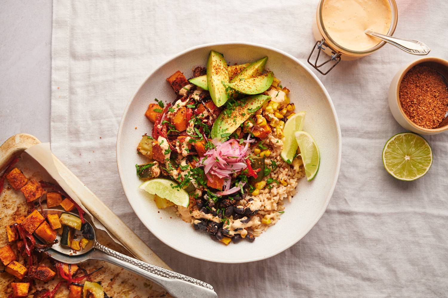 Roasted sweet potato bowls with black beans, brown rice, corn, veggies, avocado, lime wedges, and a creamy ranch dressing.