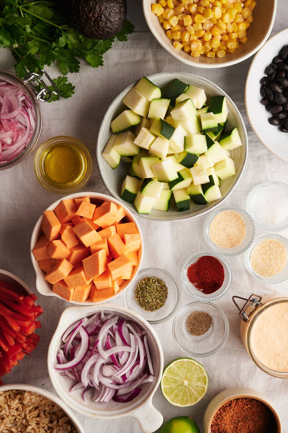 Ingredients for sweet potato bowls including diced sweet potatoes, zucchini, black beans, onion, peppers, rice, and spices.