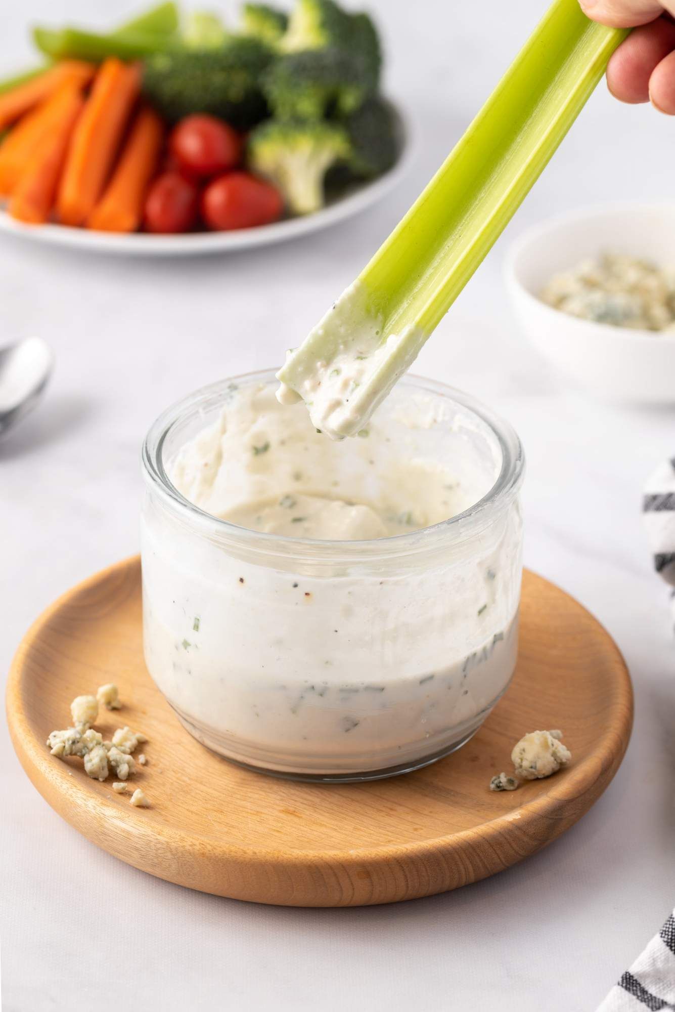 Blue cheese dressing made with yogurt in a glass jar with blue cheese crumbles and raw cut vegetables.