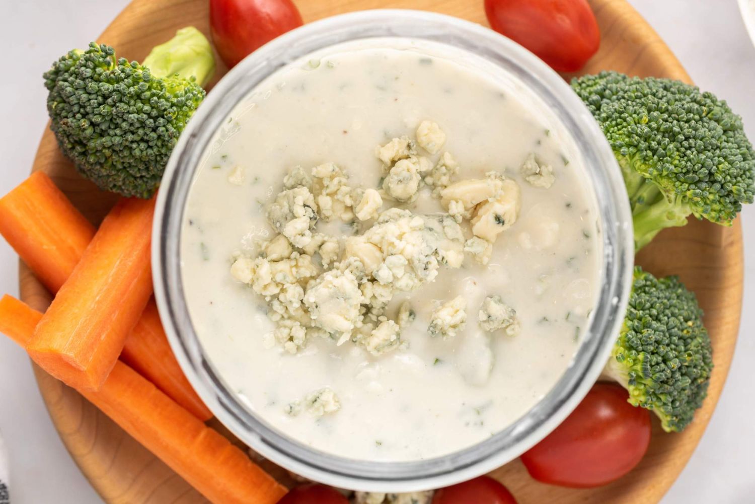 Creamy blue cheese salad dressing with raw vegetables on the side and blue cheese crumbles on top.