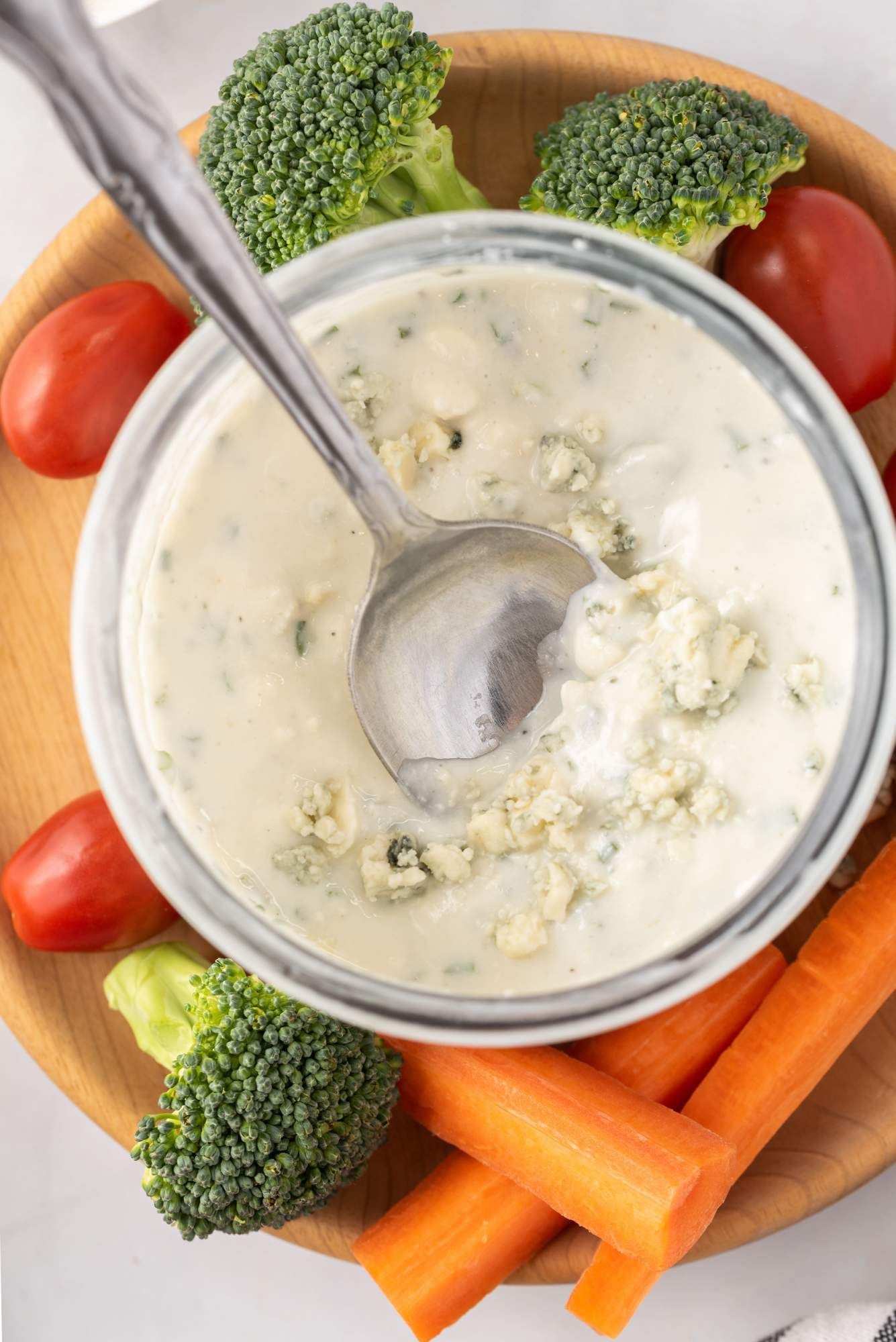 Yogurt dressing with blue cheese, garlic, and chives in a small glass jar served with carrots, broccoli, and peppers.