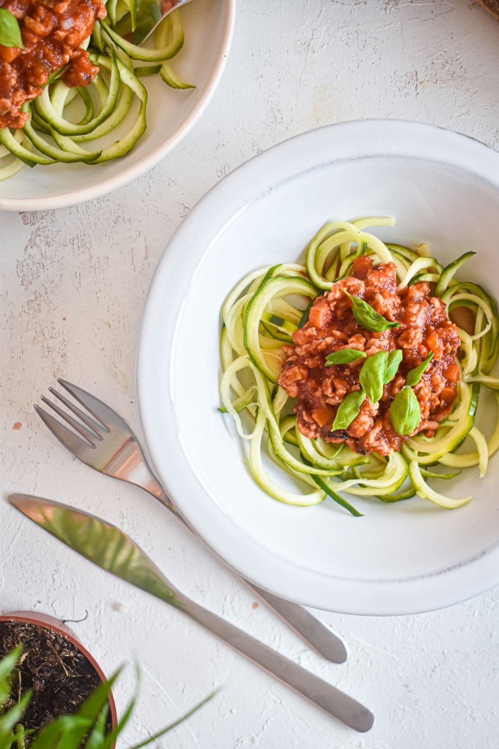 Zucchini noodle bolognese on a white plate with zucchini noodles, tomato and turkey bolognese sauce, and fresh basil.