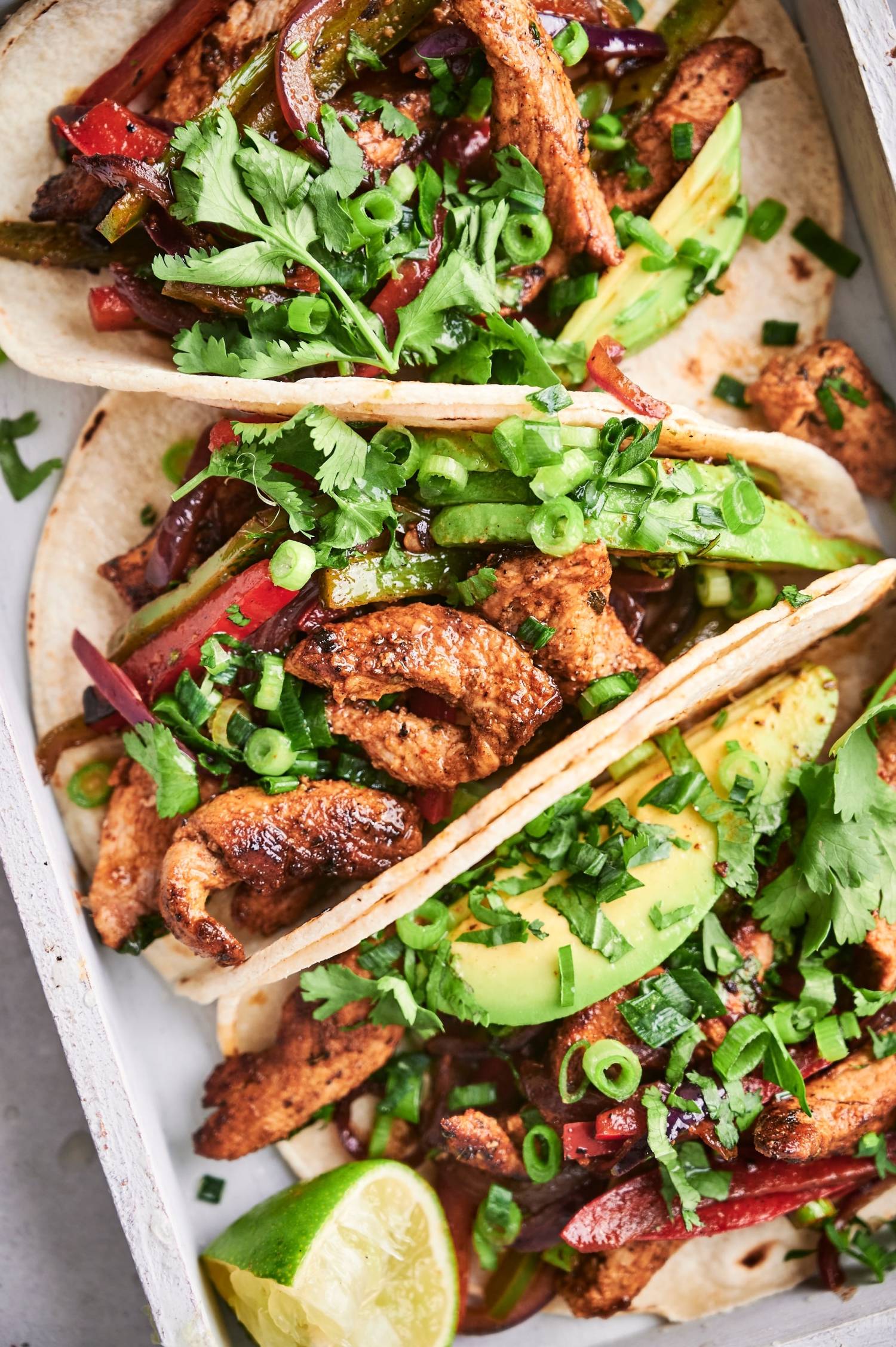 Easy pork fajitas with seasoned pork tenderloin, bell peppers, and onion served in tortillas with sliced avocado and cilantro.