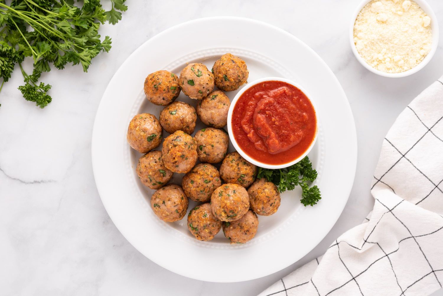 Baked turkey meatballs served on a white plate with marinara sauce on the side.