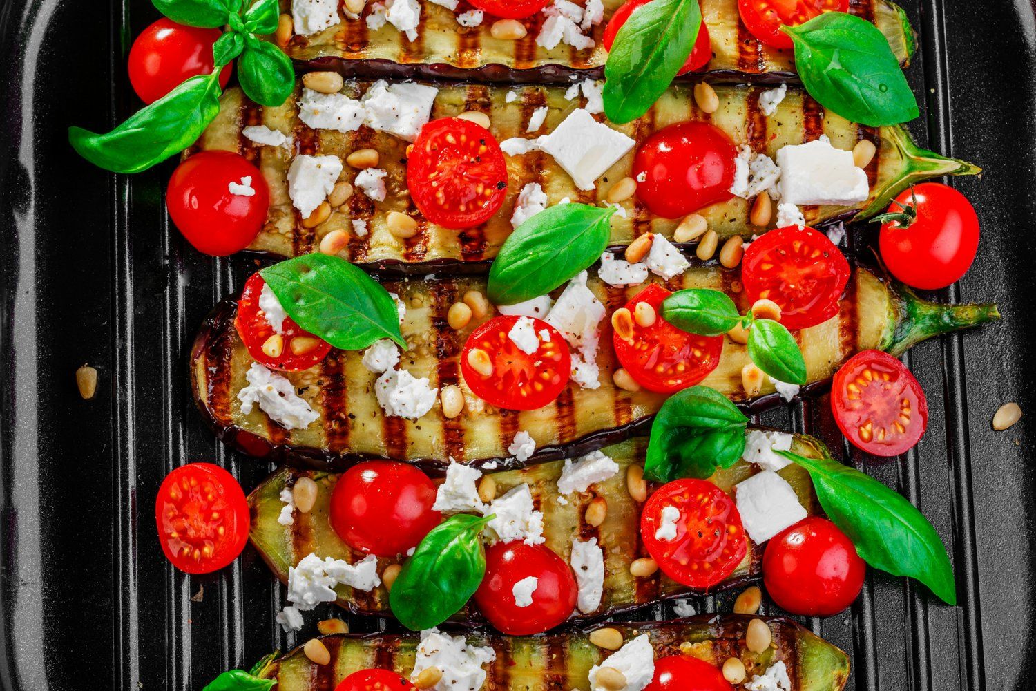 Grilled eggplant recipe on a grill pan with tomatoes and cheese.