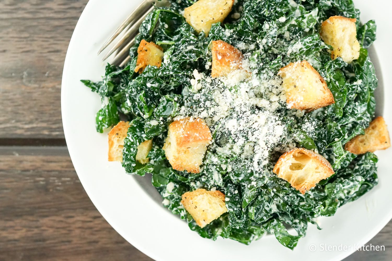 Healthy Kale Caesar with croutons and parmesan cheese on a plate on a wooden table.