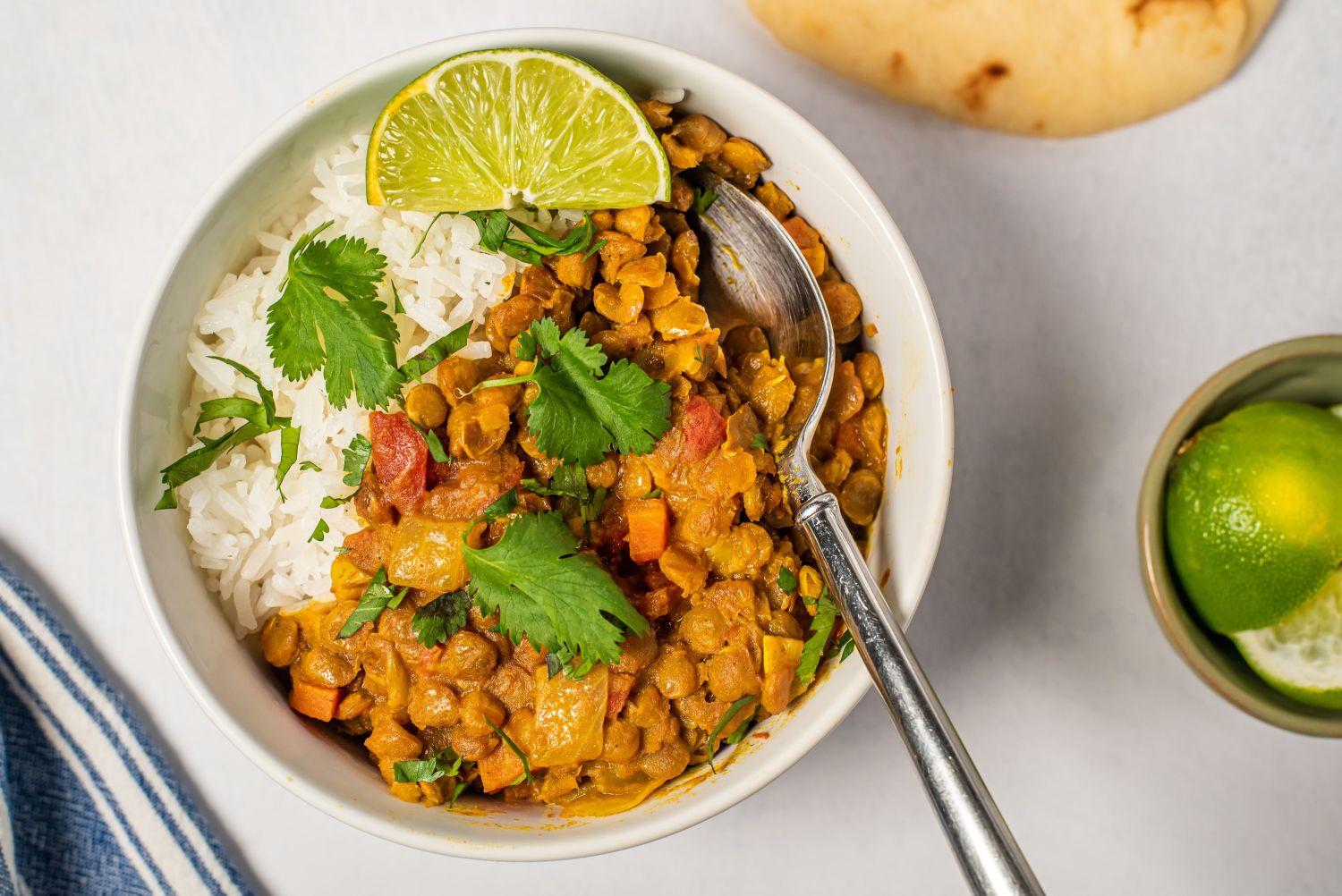 Crockpot lentil coconut curry with bell peppers and cilantro in a bowl with lime on the side.