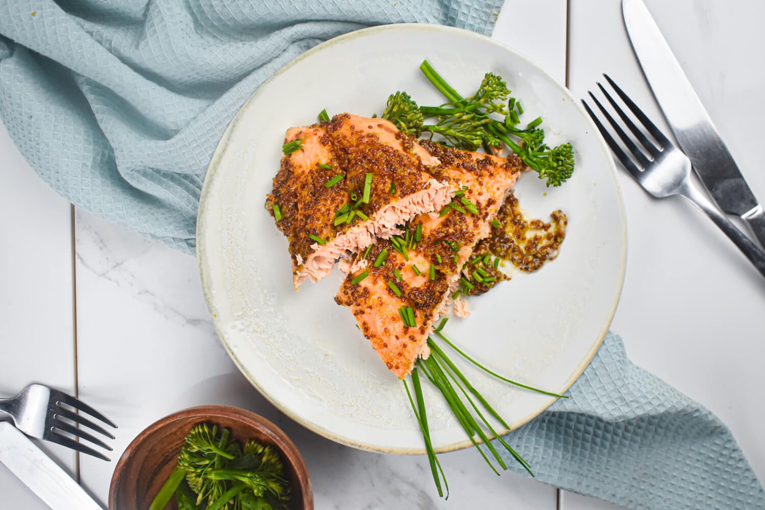 Baked salmon with a maple syrup and whole grain mustard glaze on a plate with broccoli and herbs.