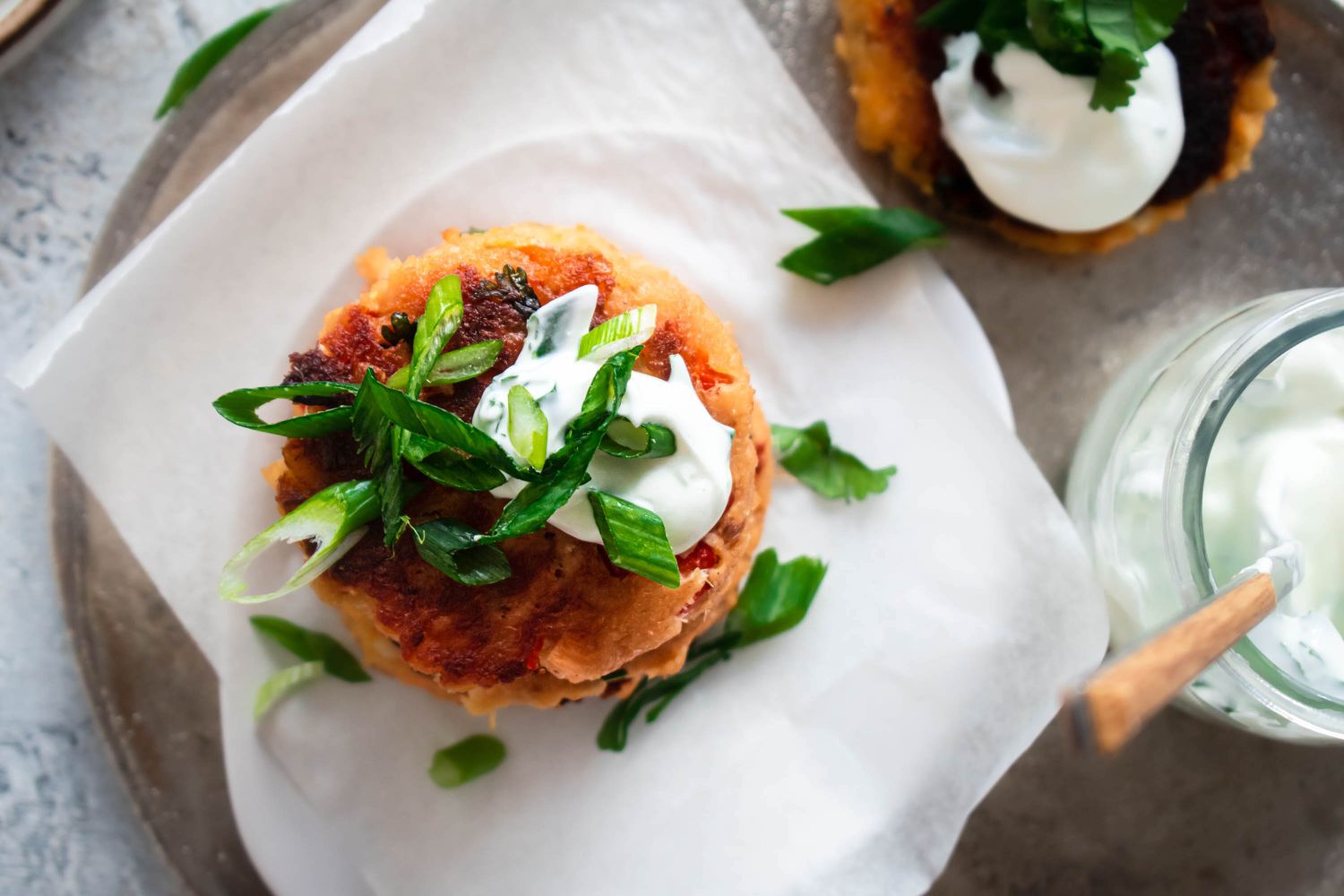 Salmon patties topped with Greek yogurt and chives on a plate with parchment paper.