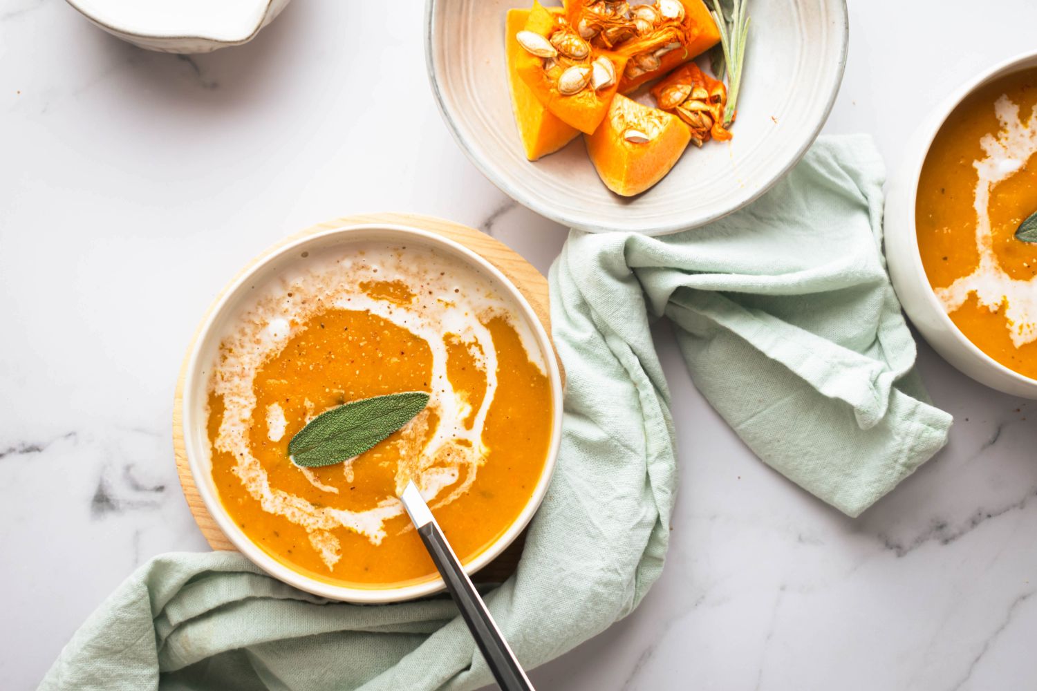 Slow cooker butternut squash soup with a swirl of cream in a bowl with sage.