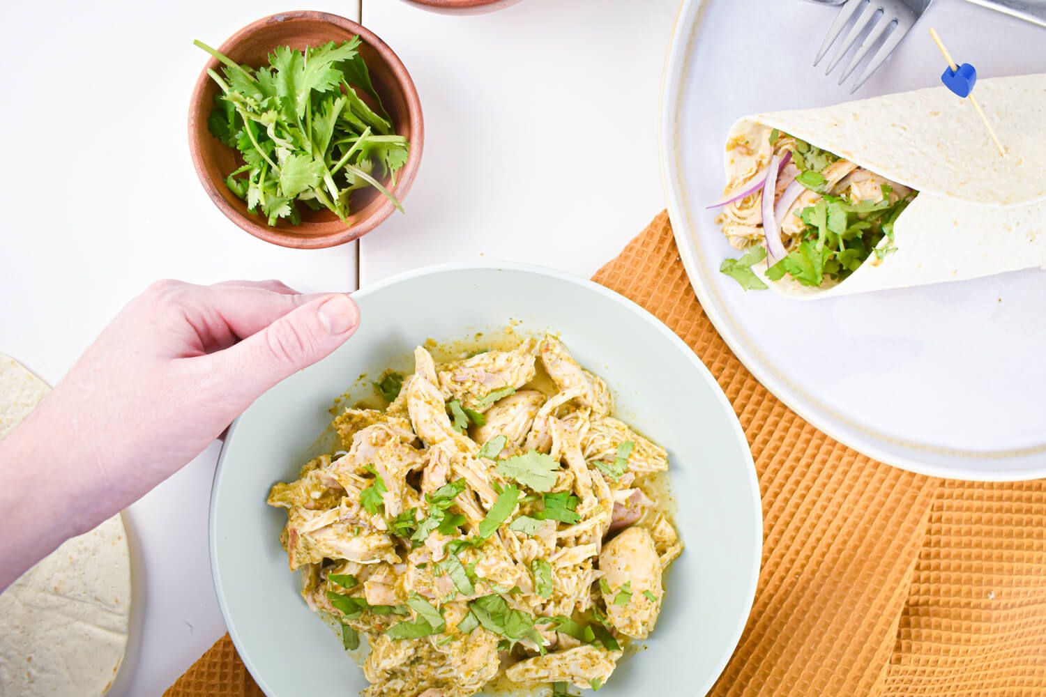 Slow cooker salsa verde chicken thighs shredded in a bowl with cilantro.