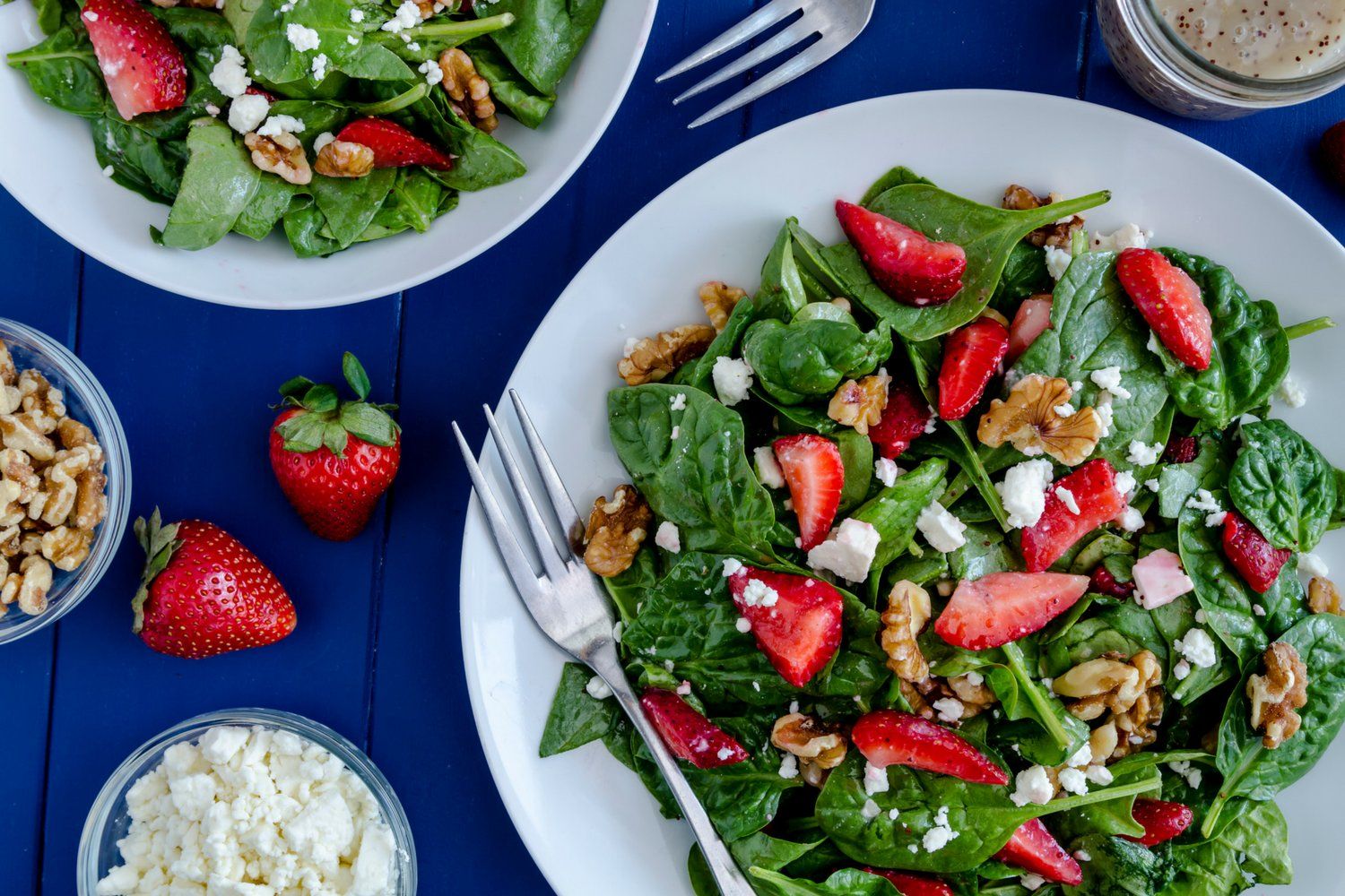 Strawberry spinach salad with feta cheese and walnuts on a blue table.