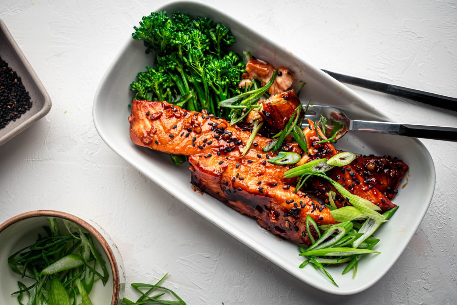 Baked teriyaki salmon in a baking dish with black sesame seeds and broccoli.