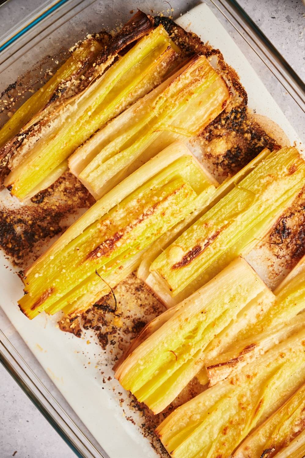 Leeks that are roasted and served in a glass baking dish with Parmesan cheese.