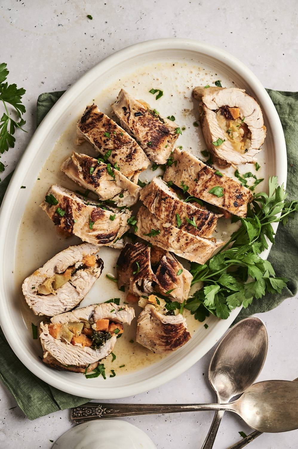 Stuffed and sliced turkey tenderloin on a large white serving dish with two spoons.