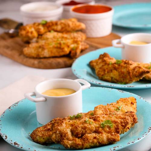 Air fryer chicken tenders with honey mustard sauce on two blue plates.