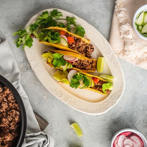 Ground beef tacos with ancho chili seasoning served in baked taco shells with lettuce, tomato, and cilantro.