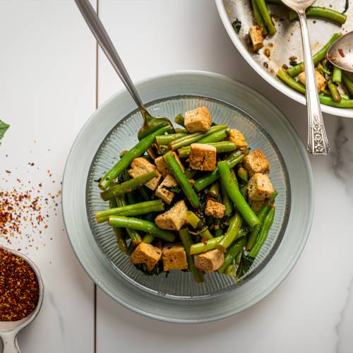 Basil tofu with green beans in a glass bowl with a skillet on the side.