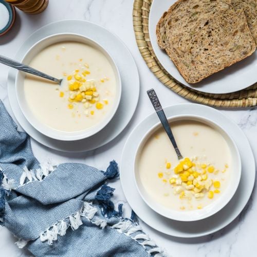 Corn chowder made with fresh corn, cauliflower, onions, milk, and spices in two bowls with bread on the side.