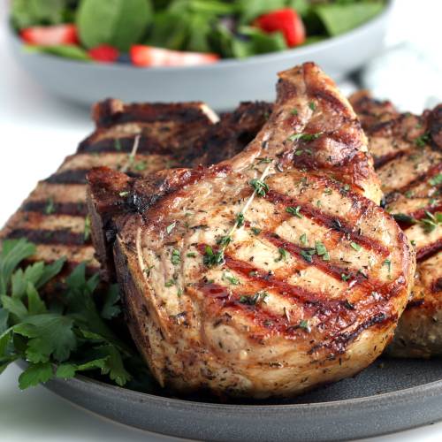 Grilled pork chops with grill marks and fresh thyme on a plate.