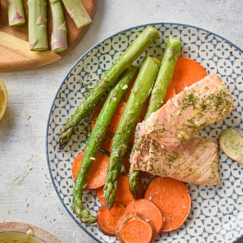 Sheet pan roasted salmon with sweet potatoes and asparagus on a plate with lemon Dijon sauce.