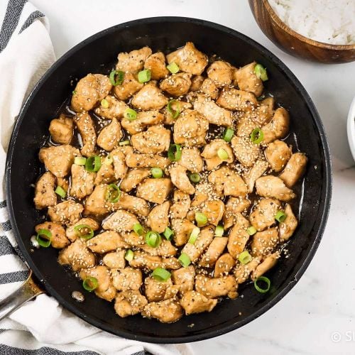 Sesame Chicken in a skillet with green onions with white rice and broccoli on the side.