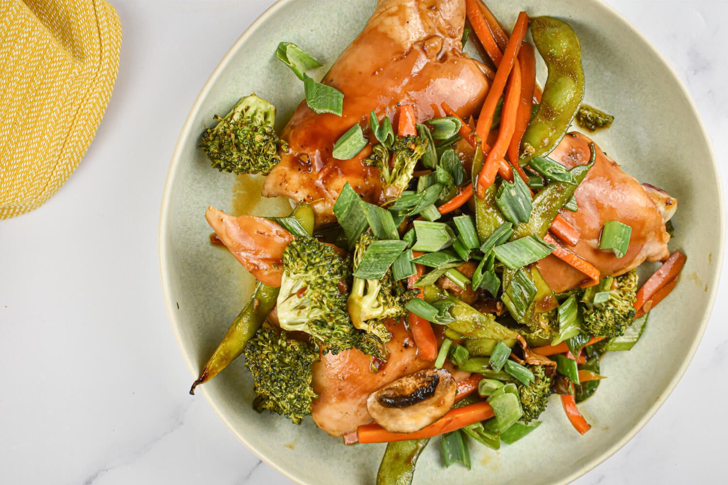 Teriyaki chicken and vegetables in a bowl with chicken thighs, carrots, broccoli, snap peas, and green onions.