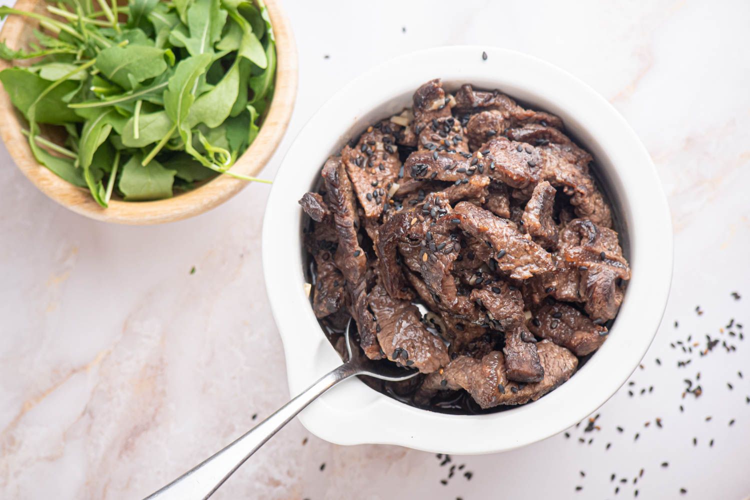 Sesame beef with thinly sliced flank steak in a sesame sauce in a bowl with sesame seeds.