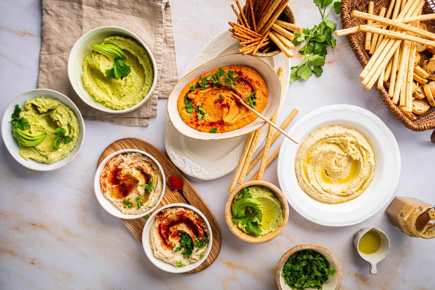 Hummus in bowls including classic hummus, avocado hummus, roasted red pepper hummus, and garlic hummus.