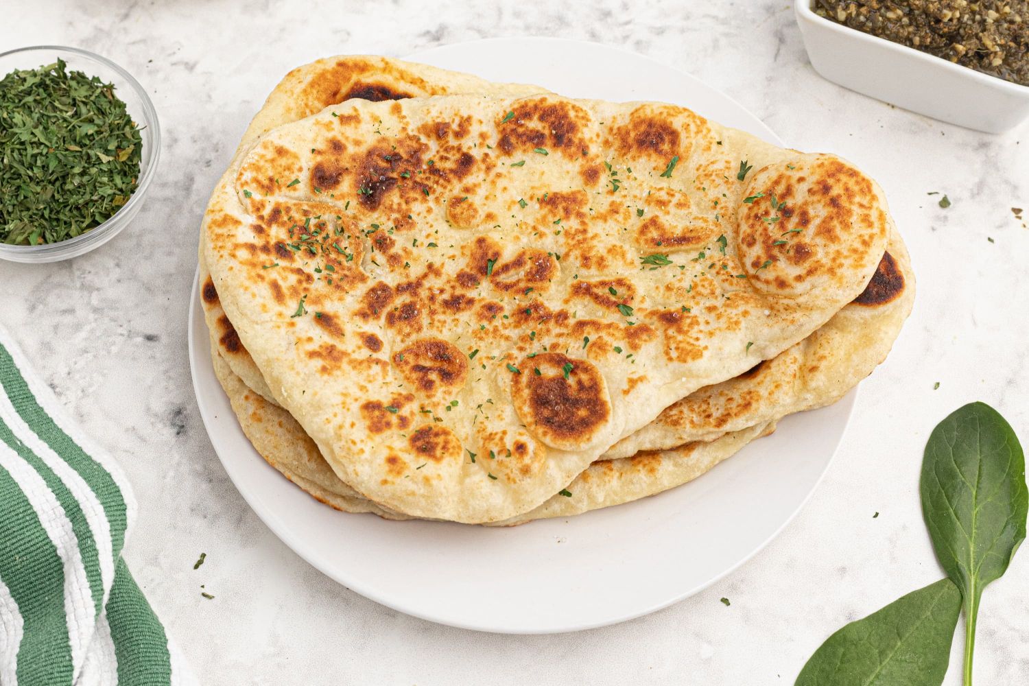 Homemade Naan with some charred edges on a plate with spinach on the side.