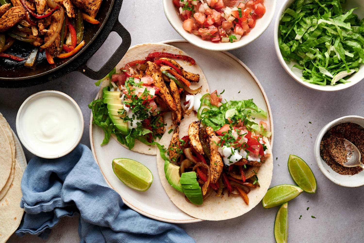 Fajita tacos with chicken breast, peppers, onions, sour cream, avocado, and salsa in corn tortillas.