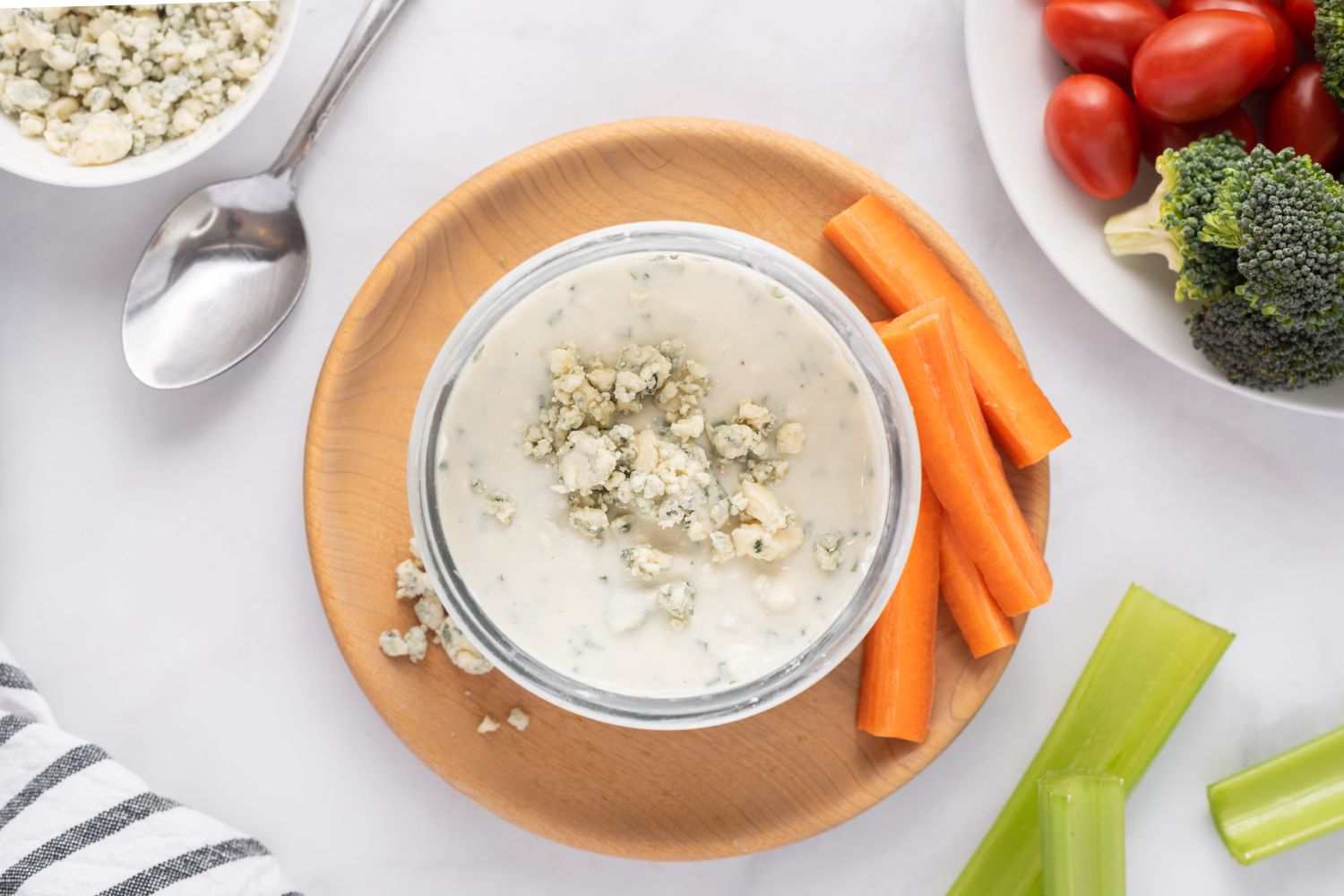 Yogurt blue cheese dressing with crumbled blue cheese in a glass bowl with raw vegetables on the side.