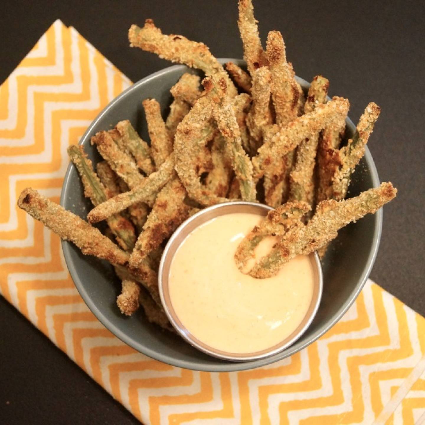 Green bean fries in a bowl with a crispy coating and sauce on the side.