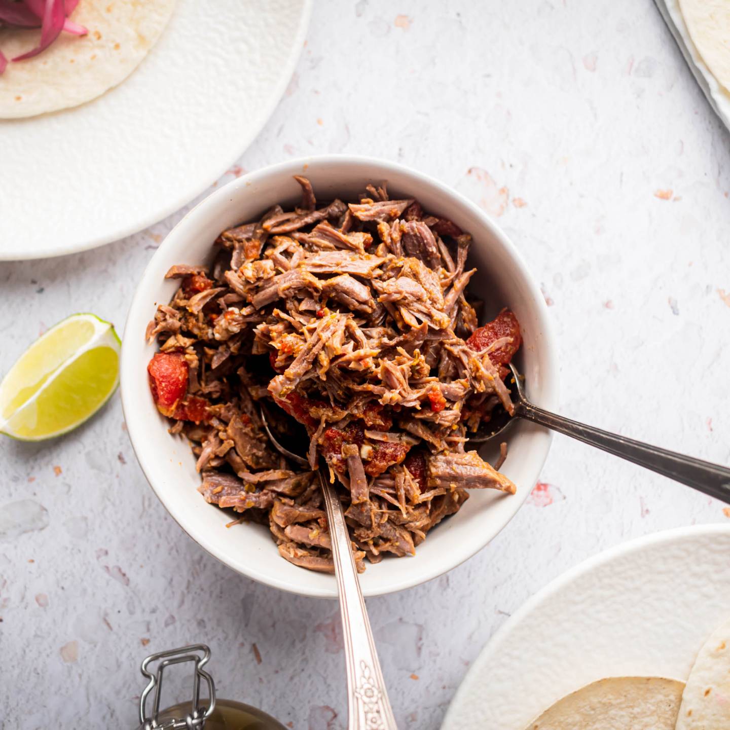 Mexican shredded beef in a bowl with tomatoes and chipotle peppers with tacos on the side.