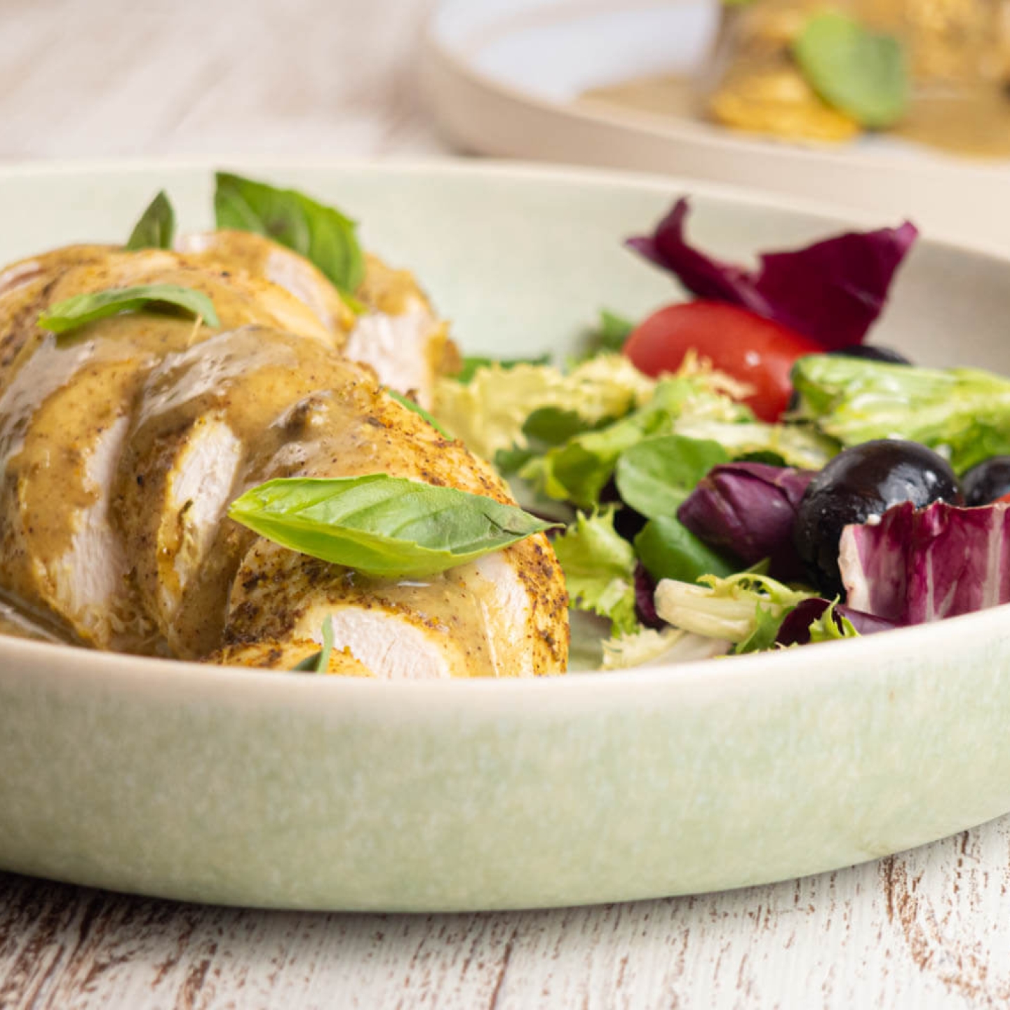 Slow cooker coconut basil chicken on a plate with creamy sauce and salad on the side.