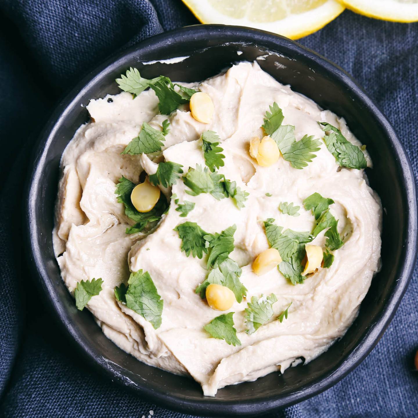 Artichoke hummus with lemon and chickpeas in a bowl with a blue napkin.