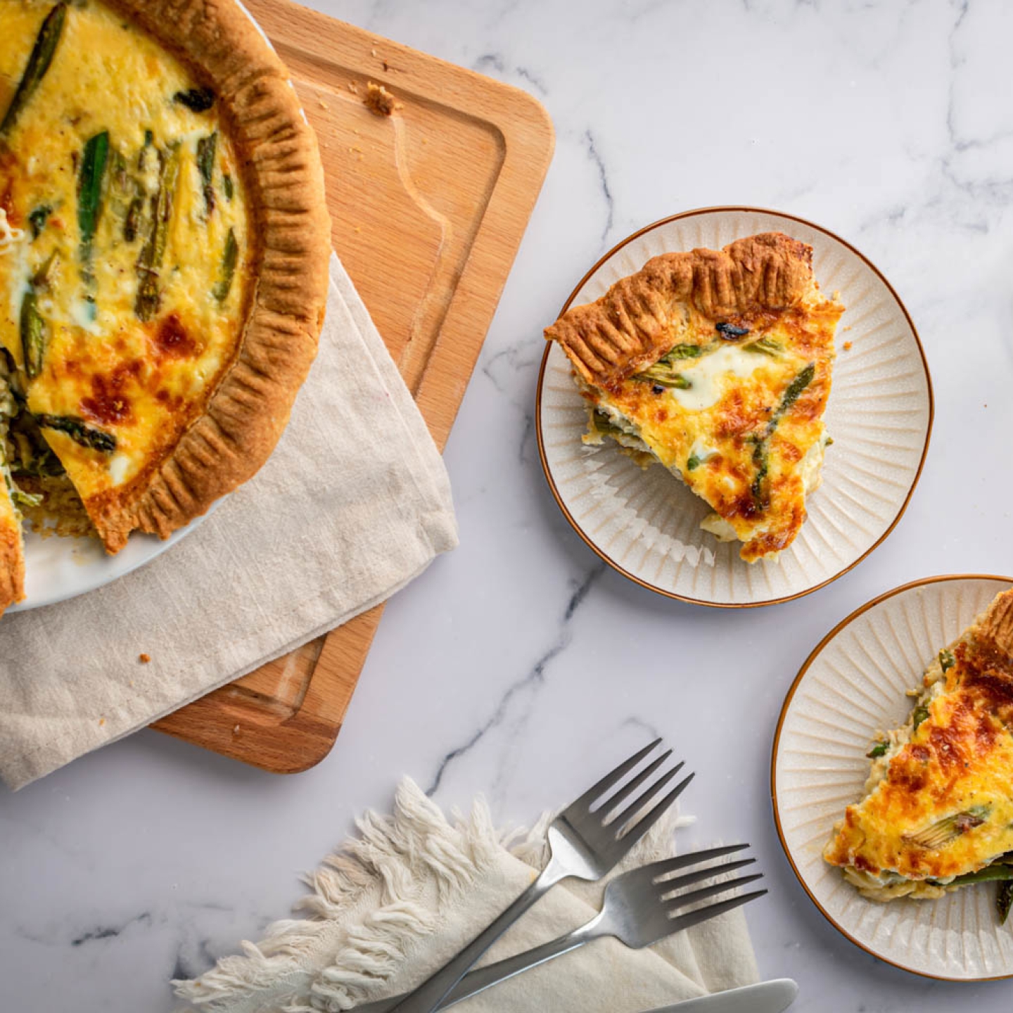 Asparagus quiche with eggs, shredded cheese, asparagus, and red onions cooked in a golden brown crust and served on plates.